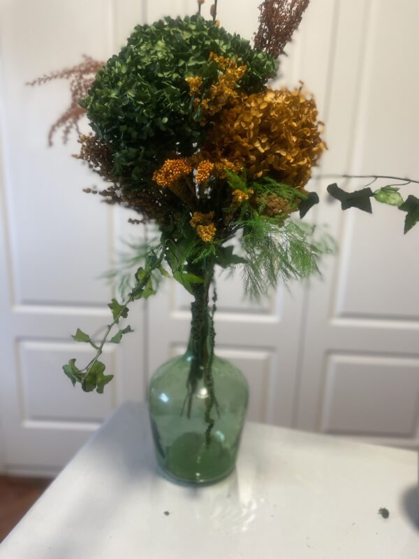 Damajuana con arreglo floral en tonos verdes y naranjas